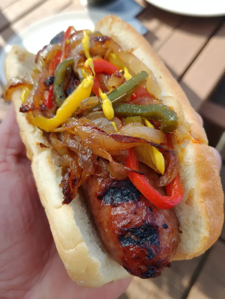 Smartphone photo of a Grilled Kielbasa Sandwich being held over an outdoor wooden table in natural light.
