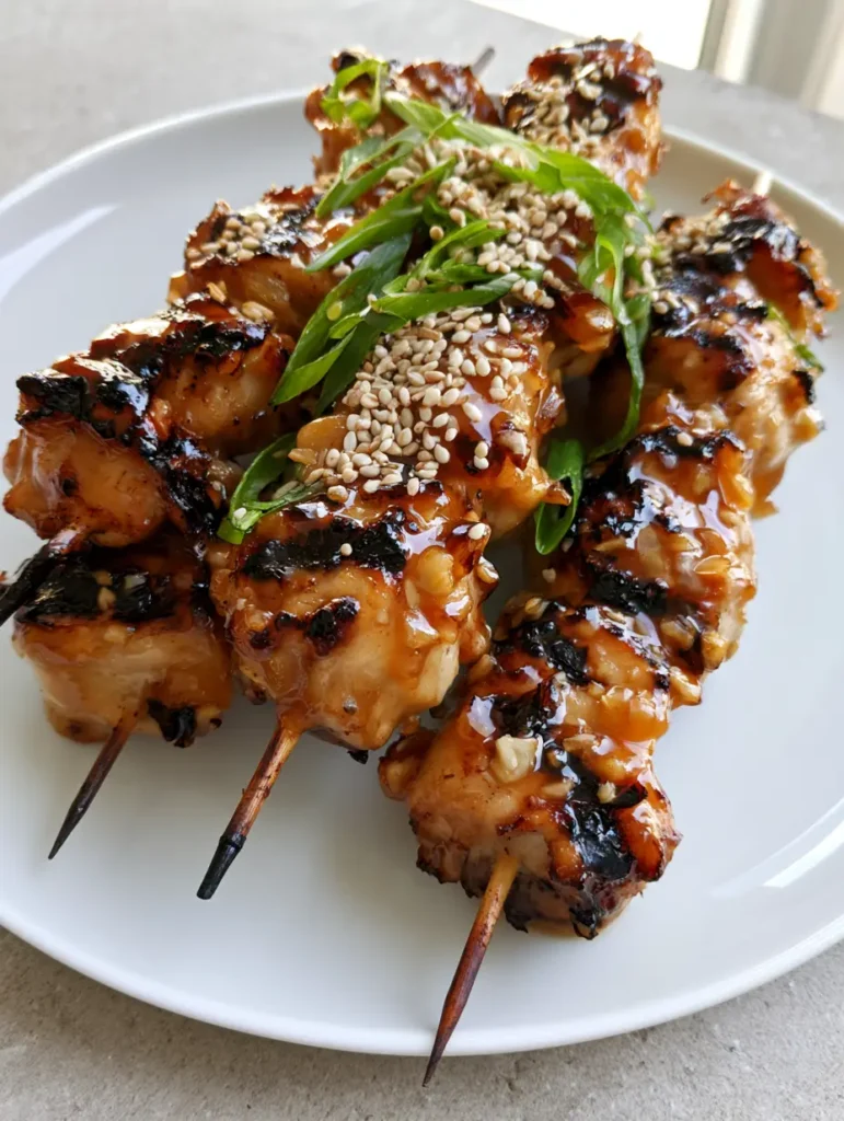 Honey Garlic Chicken Skewers: The Ultimate Sticky Grilled Dinner 2 Handheld photo of Honey Garlic Chicken Skewers with visible minced garlic and charred grill marks on a white plate.