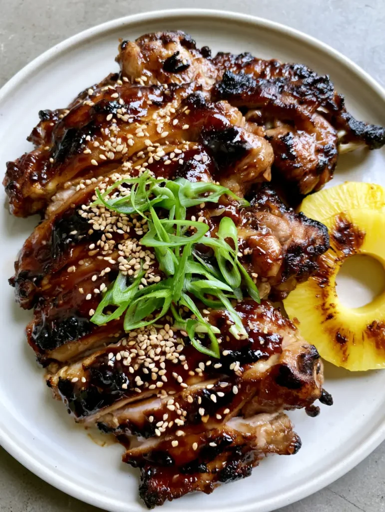 Top-down view of grilled chicken thighs with a thick glossy amber glaze and charred edges. (Hawaiian Teriyaki Chicken)