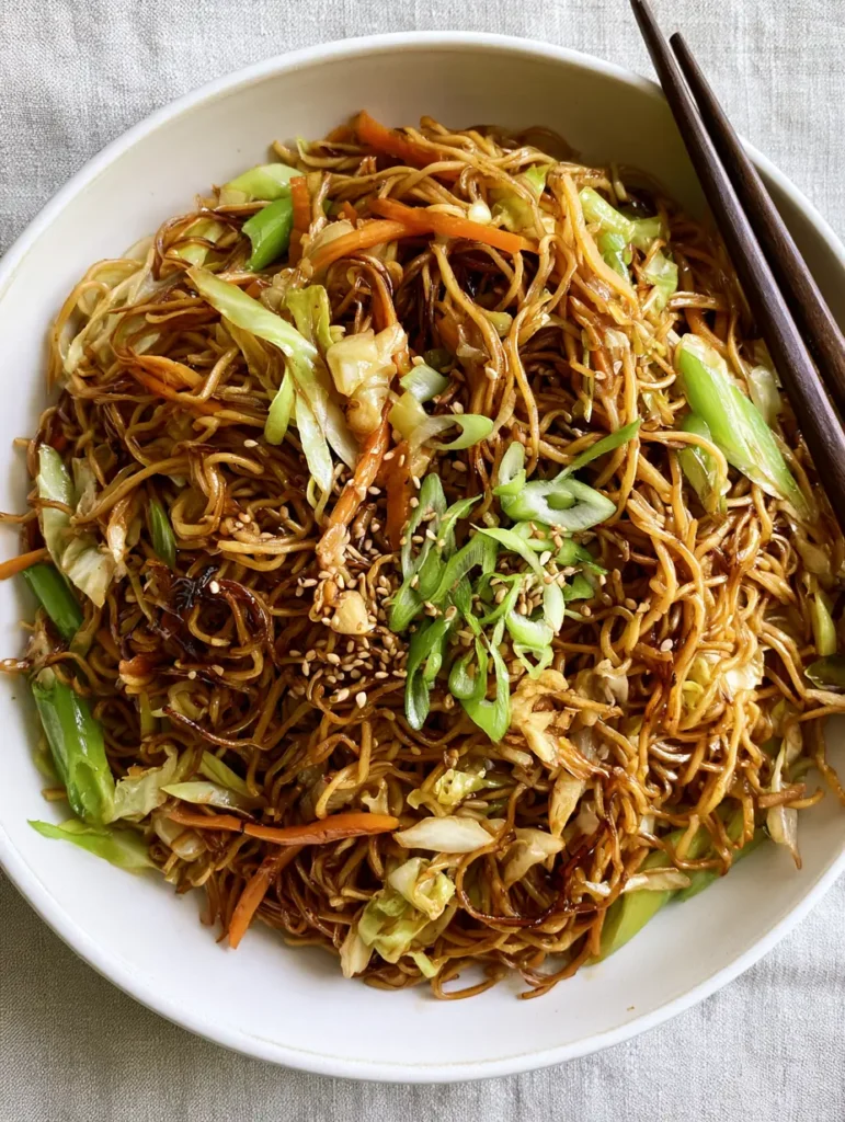 Easy Chow Mein Recipe: The Ultimate 20-Minute Glossy Stir-Fry 2 Close up of thin wheat noodles in a dark soy glaze with green cabbage ribbons and orange carrots. (Easy Chow Mein Recipe)