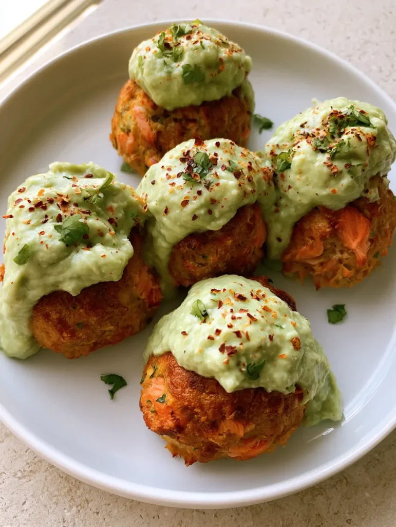 A macro shot of pink salmon flakes inside a golden-brown meatball with avocado sauce clinging to the side.