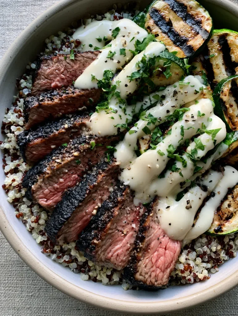 Grilled Steak Bowl with Creamy Garlic Sauce and Charred Zucchini 2 A handheld smartphone photo of a Grilled Steak Bowl with medium-rare steak slices, grilled zucchini, and parsley garnish in a ceramic bowl.