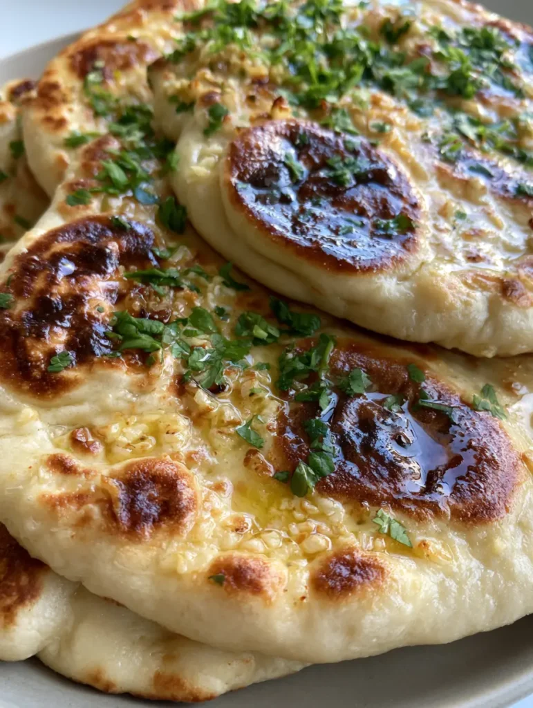 Stack of warm naan bread with glistening melted salted butter and minced fresh garlic.