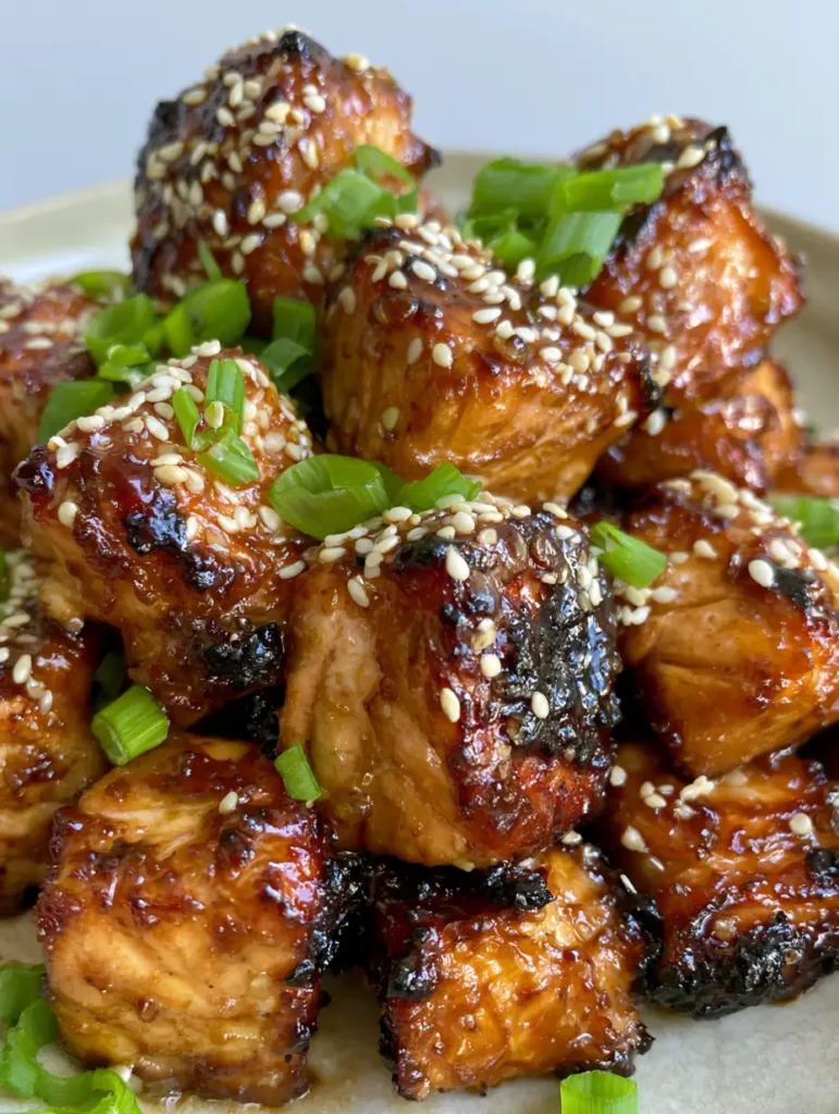 Overhead view of Honey Garlic Salmon Bites topped with sesame seeds and green scallions on a light-colored background.