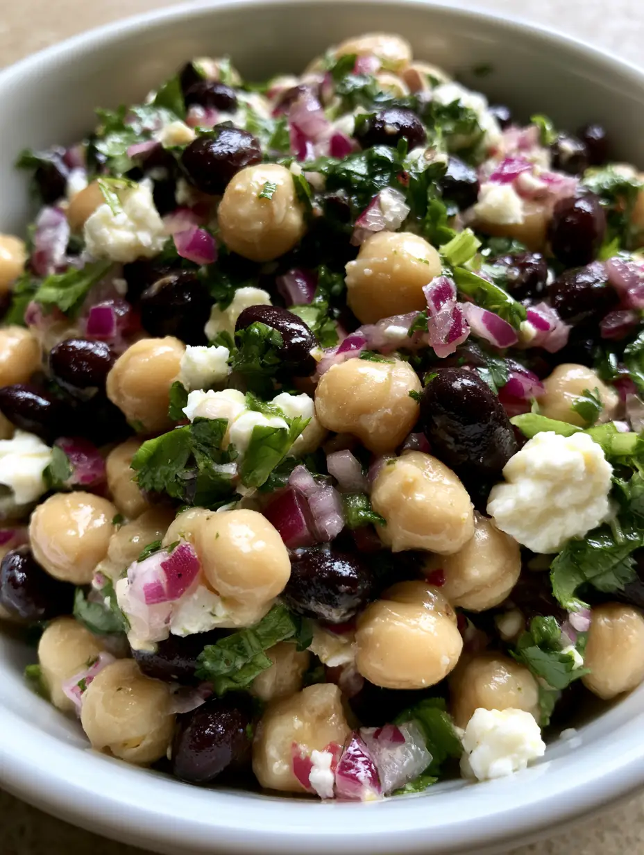 Close-up of a Chickpea and Black Bean Salad showing glossy lime dressing, beige chickpeas, and matte black beans with red onion.