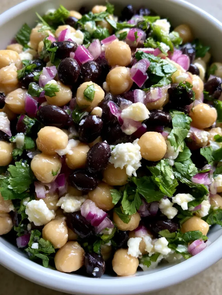 Top-down view of Chickpea and Black Bean Salad emphasizing the jagged edges of white feta cheese and fresh cilantro.