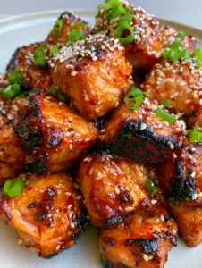 Handheld photo of bite-sized seared Honey Garlic Salmon Bites showing flaky texture and sticky amber glaze.