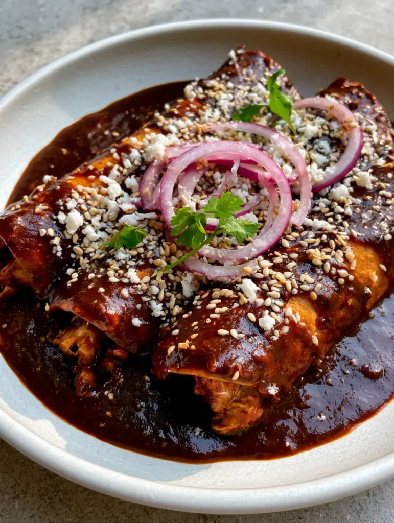 Chicken Mole Enchiladas: The Ultimate Rich and Smokey Recipe 1 Visual details of raw red onion rings and toasted sesame seeds on top of deep dark-brown mole sauce.