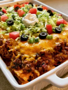 Close up shot of melted orange cheddar cheese over seasoned ground beef and golden corn chips in a white dish. (Walking Taco Casserole)