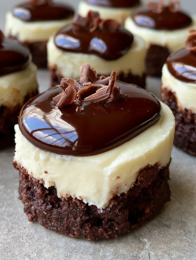 Several mini cheesecakes with glossy dark chocolate ganache pooling in the center and fine milk chocolate curls on top.
