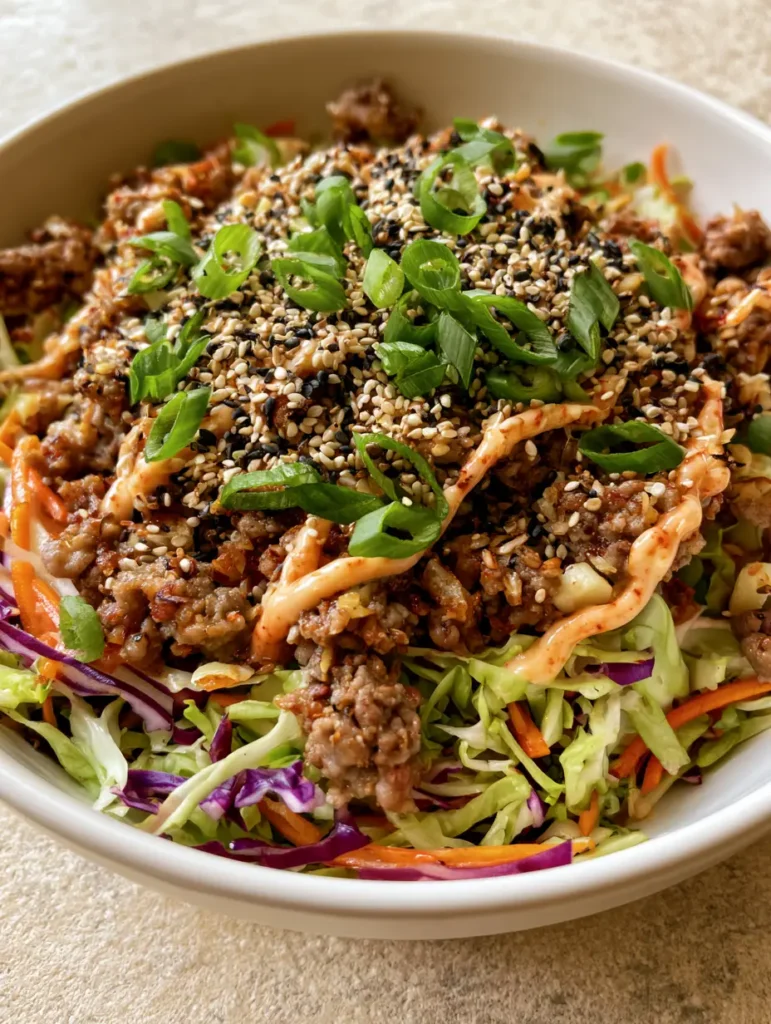 Close up shot of browned meat crumbles and julienned carrots in a High Protein Egg Roll in a Bowl.